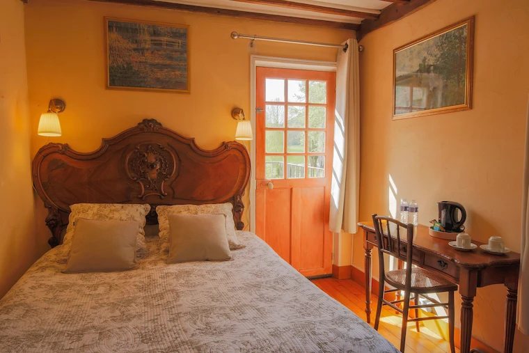 Chambre aux tons ocre et terracotta avec lit double en bois sculpté et porte ouvrant sur le jardin