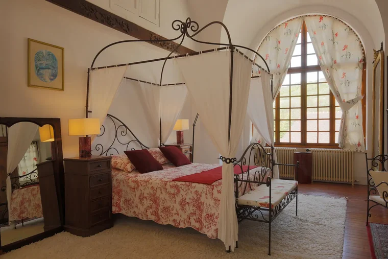Lit à baldaquin en fer forgé de la Suite Monet, habillé d'une parure toile de Jouy, devant une grande fenêtre cintrée